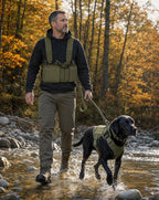 Man and black Labrador crossing a stream in matching green gear